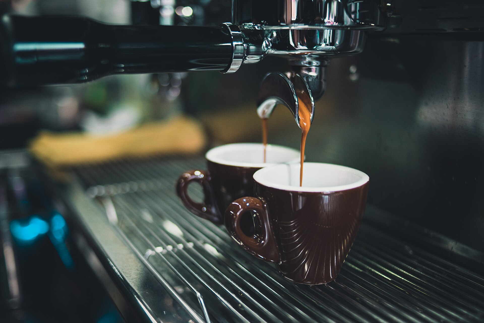 Two brown cups under an espresso machine in an Italian-style coffee bar