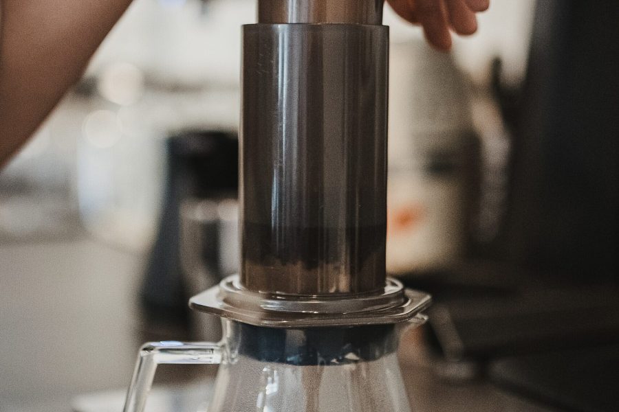 A hand pressing the plunger of an AeroPress over a glass carafe, a classic aeropress vs french press contrast