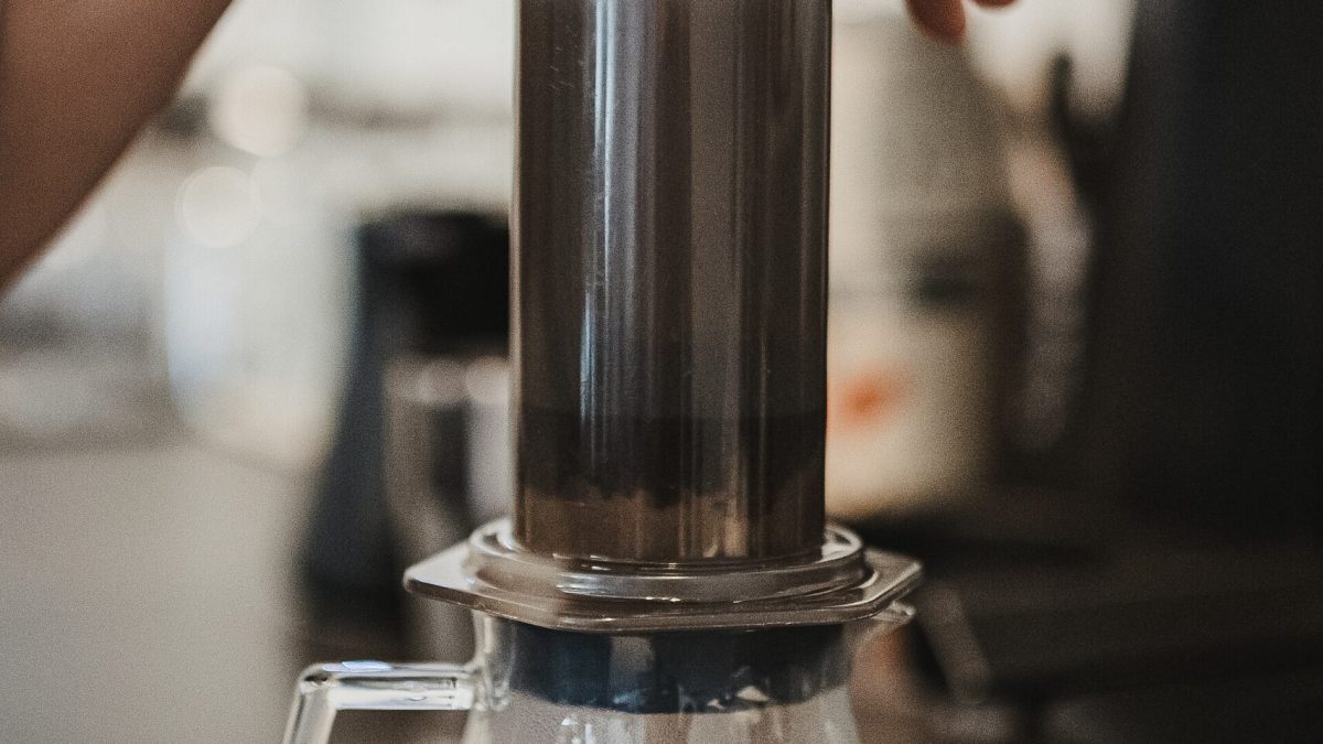 A hand pressing the plunger of an AeroPress over a glass carafe, a classic aeropress vs french press contrast